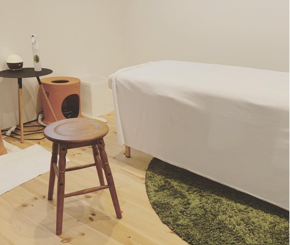 木の床に白いベッドと緑のラグがあるat feelの施術室